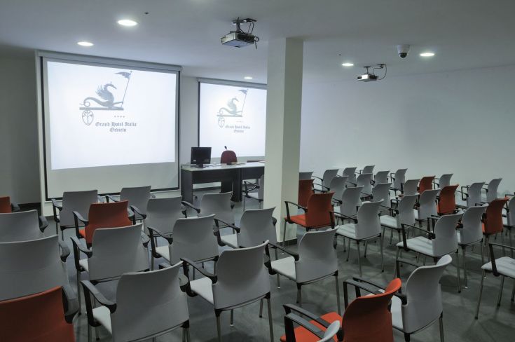 Spazio attrezzato per conferenze, con sedie disposte e strumenti audiovisivi. Ambiente sobrio e funzionale.