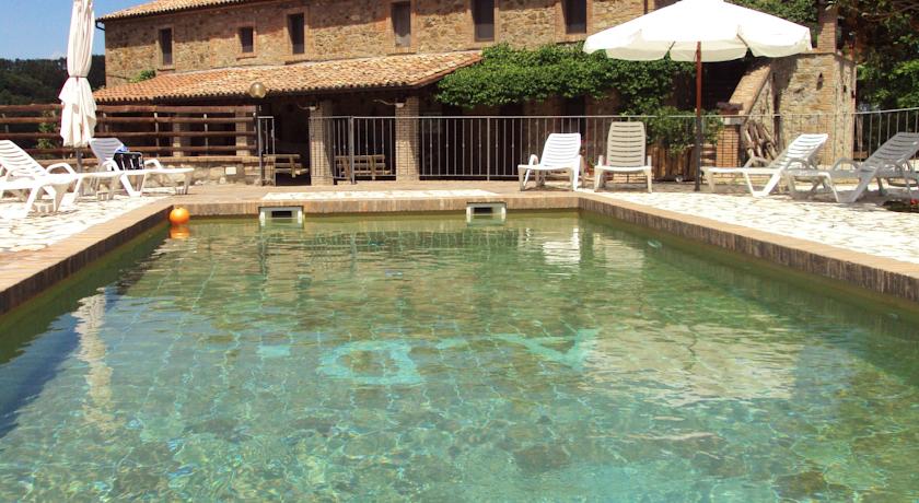 Una piscina pulita, circondata da lettini, con un grande edificio rustico sullo sfondo.