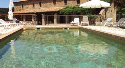 Una piscina pulita, circondata da lettini, con un grande edificio rustico sullo sfondo.
