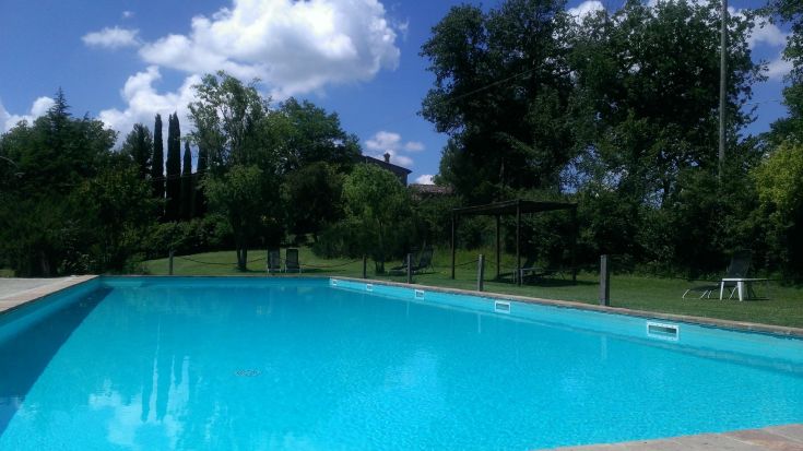 Una piscina di colore blu circondata da alberi e siepi, perfetta per godersi un momento di relax nella campagna umbra.