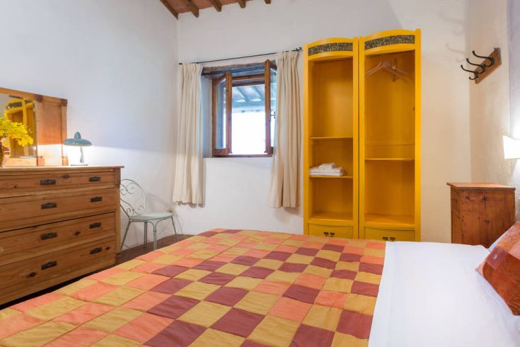 Camera semplice e accogliente con letto matrimoniale e armadio giallo, affacciata su una valle umbra.