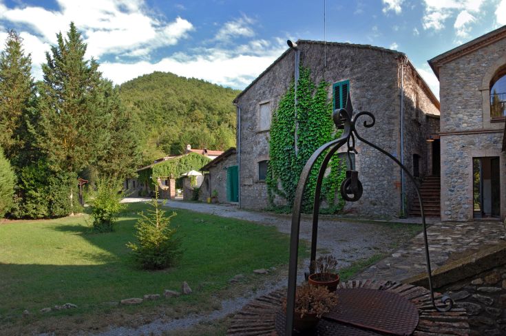 Landhaus umgeben von rustikalen Gebäuden und grünen Hügeln in einer schönen Naturlandschaft.