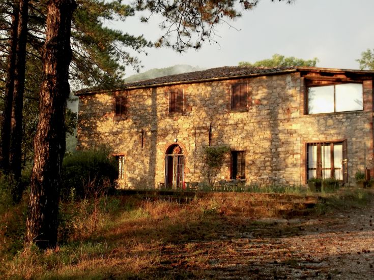 Ein historisches Gebäude in einem grünen Tal, umgeben von Bäumen und mit einer ruhigen Atmosphäre.