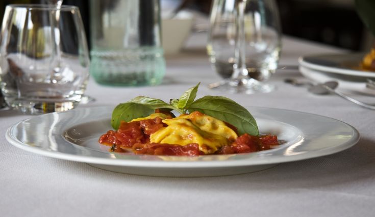 Mit einer leckeren Füllung gefüllte Ravioli, auf einem weißen Teller serviert, mit frischen Tomaten und Basilikumblättern garniert.