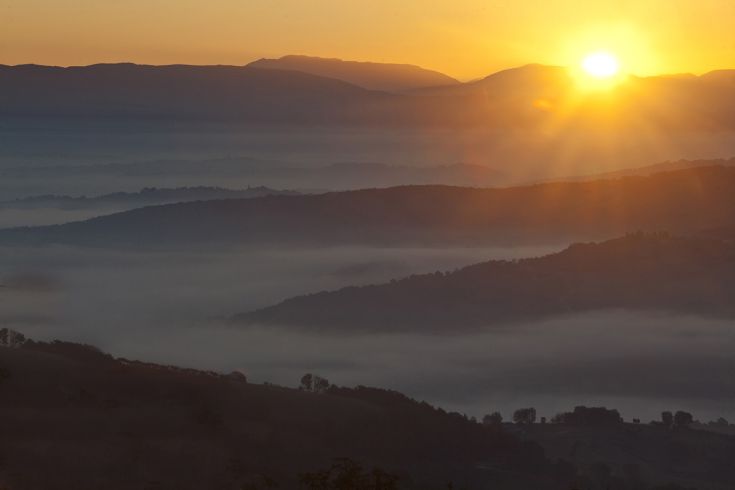 A unique dawn reflects on soft hills in a fog-covered landscape.