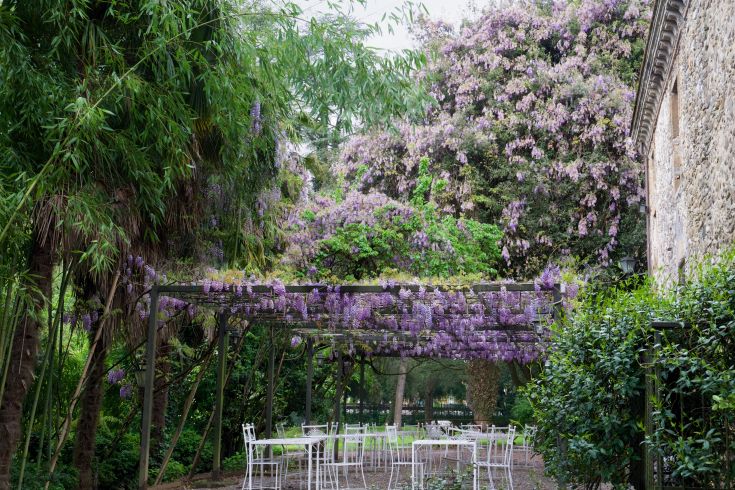 Giardino con pergolato di glicini e tavoli bianchi, adatto per momenti di tranquillità all'aperto.