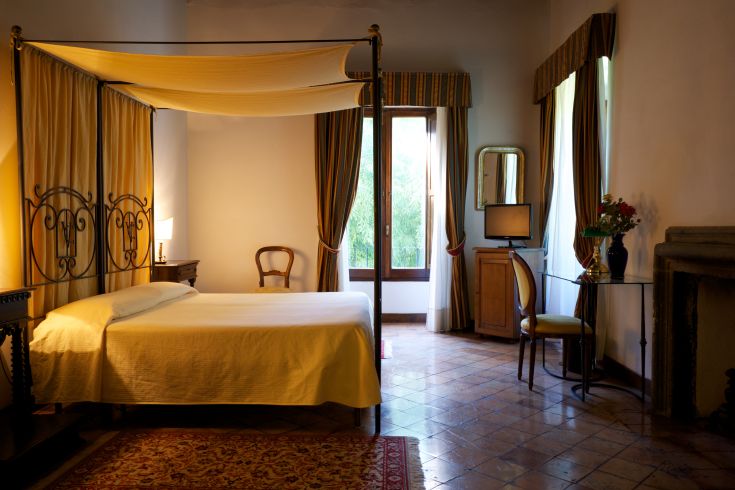 Camera con letto a baldacchino, illuminazione calda e affaccio su un parco. Luogo adatto per un soggiorno tranquillo.