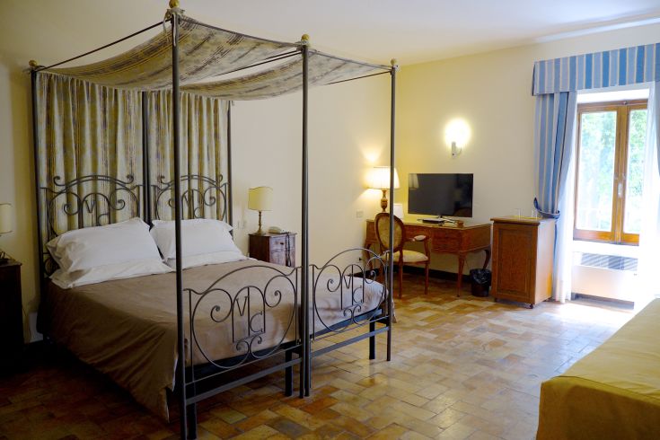 Camera confortevole con letto a baldacchino, dotata di arredi classici e illuminazione naturale. Spazio accogliente.