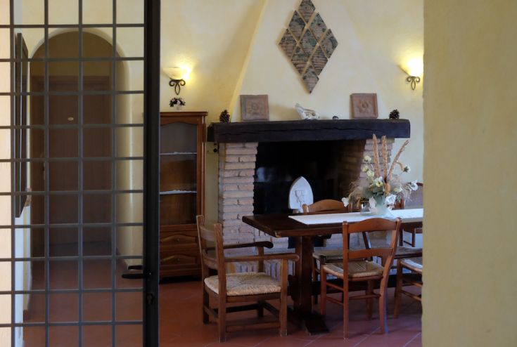 Spazio interno semplice con tavolo e camino, adatto per momenti di condivisione.