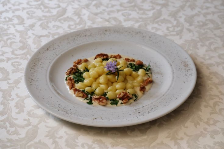 Gnocchi serviti con noci e fiori edibili, disposti in modo semplice ma curato.