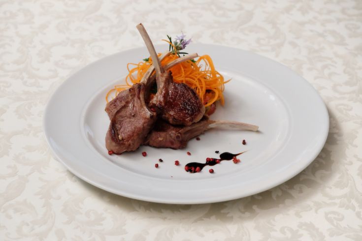 Piatto di costolette d'agnello servito con carote e salsa.