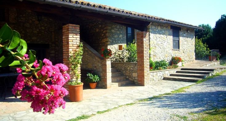 Un edificio in pietra immerso in un paesaggio verde, con fiori colorati che adornano l'area circostante.