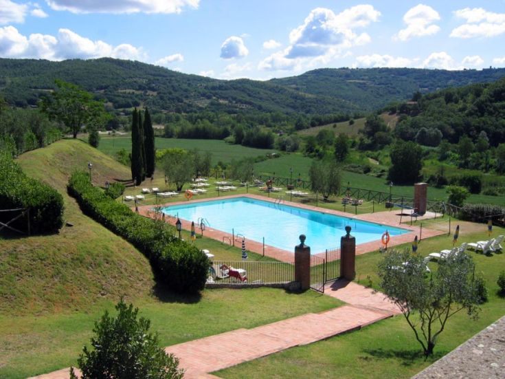 Scena della piscina circondata da colline e vegetazione, immersa nel verde della natura.
