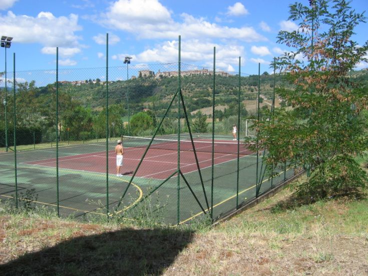 Un campo da tennis situato in un'area verde, con due giocatori che stanno giocando.