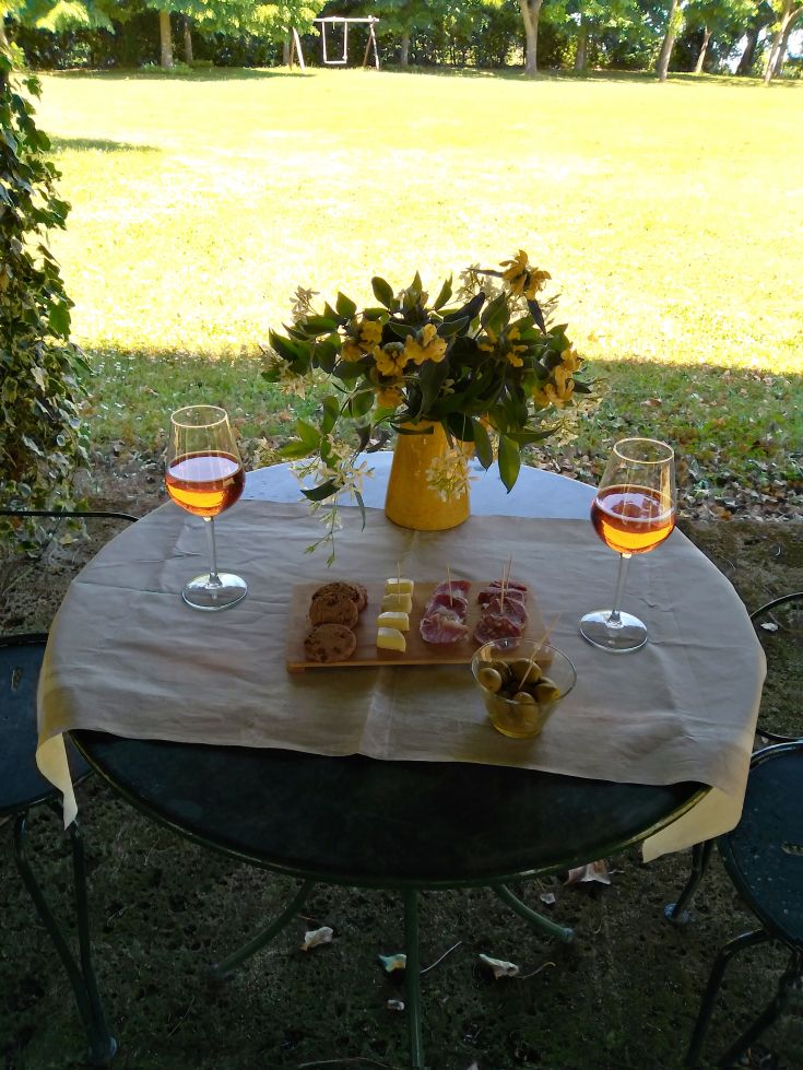 Ein Tisch im Freien mit Wein, Essen und Blumen in natürlicher Umgebung.