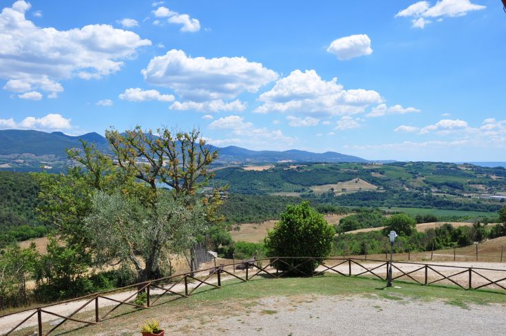 Scene of the Umbrian countryside featuring green hills and clouds in a clear sky.