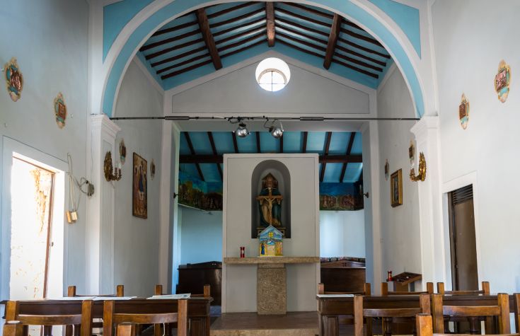 Interno di una chiesa con soffitto blu e decorazioni, sedie in legno e un'atmosfera tranquilla.