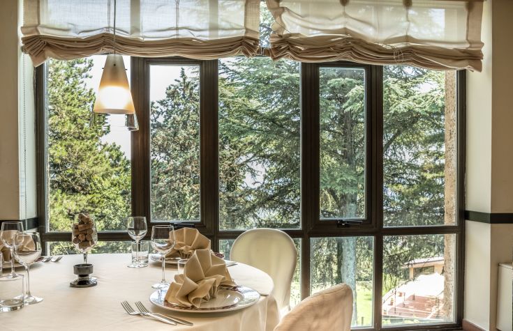 Scena tranquilla di un ristorante elegante, incorniciato da alberi, con un tavolo accuratamente apparecchiato.