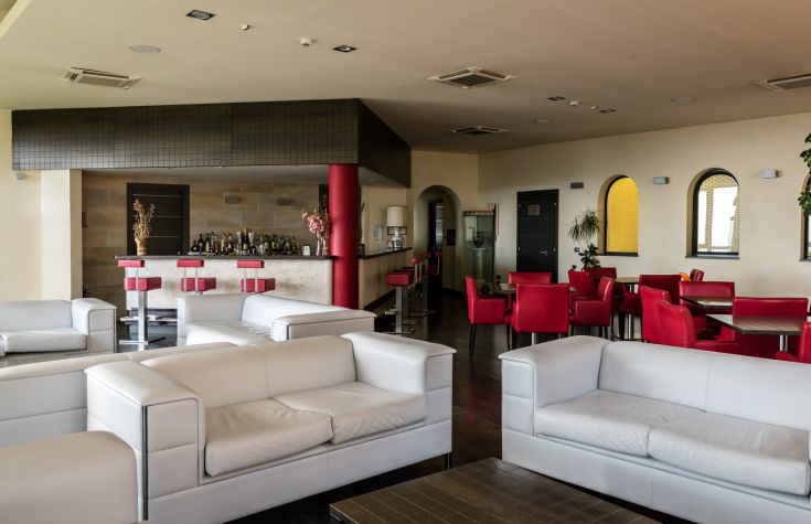 Lounge dell'hotel con divani bianchi e elementi decorativi rossi, ambiente adatto al relax.