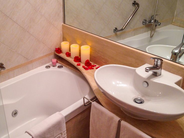 Un bagno semplice e raffinato con vasca, arredato con candele e petali di rosa per un'atmosfera accogliente.