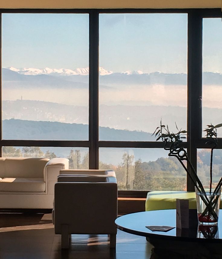 Panorama dalle ampie finestre di un hotel, che mostra dolci colline e montagne in lontananza.