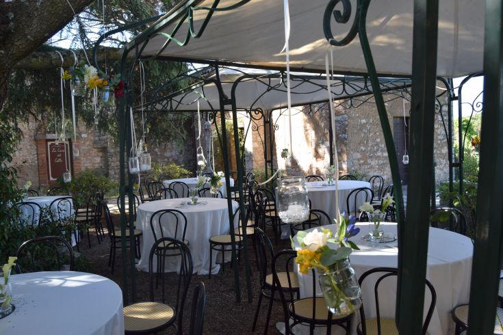 Un'area verde all'aperto con tavoli bianchi e fiori, adatta per eventi e cerimonie. Spazio tranquillo e ben curato.