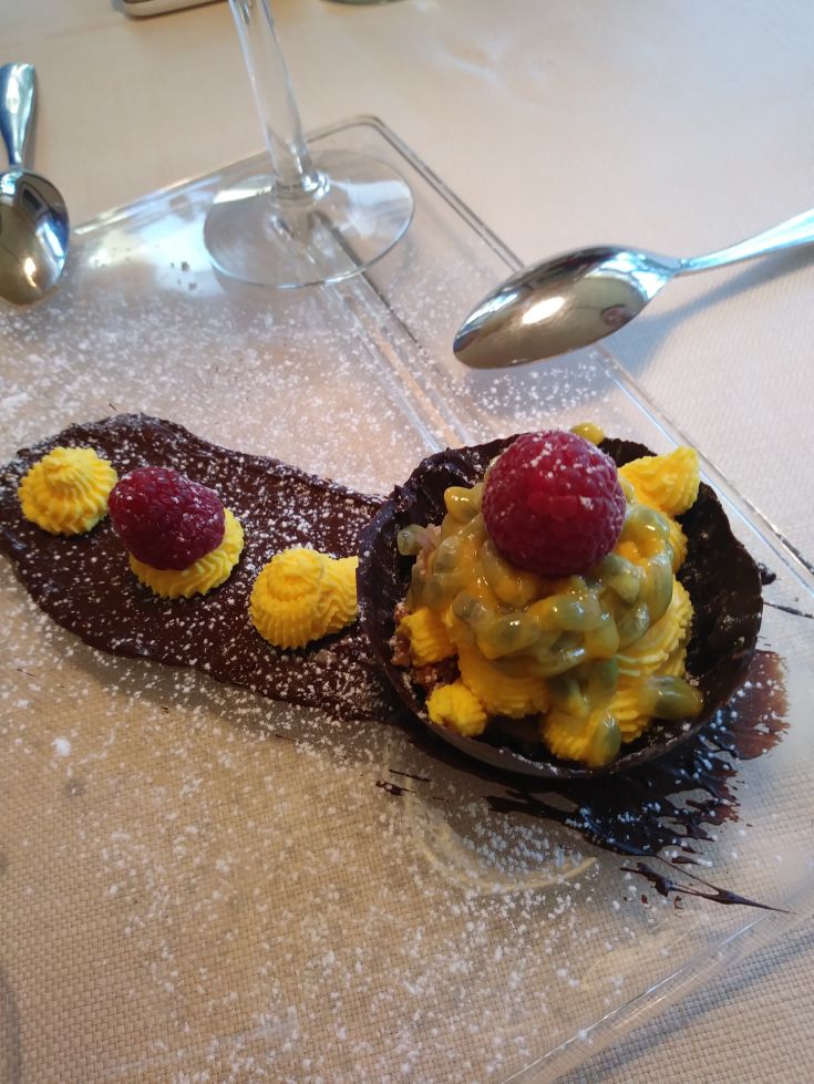 Un dessert al cioccolato servito con frutti di bosco freschi e una leggera crema al frutto della passione.