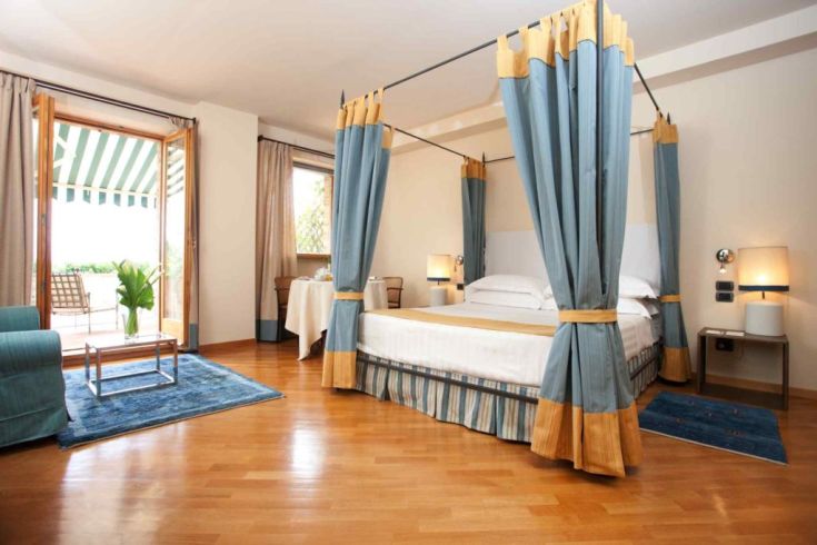 Room with a canopy bed, simple decor, and a view of the hills. Cozy and informal atmosphere.