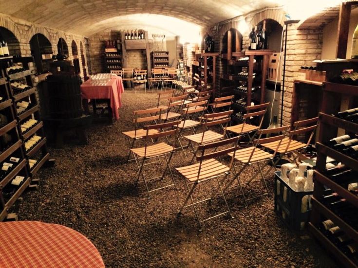 A cozy wine cellar with shelves filled with wine bottles and wooden chairs, perfect for tastings.
