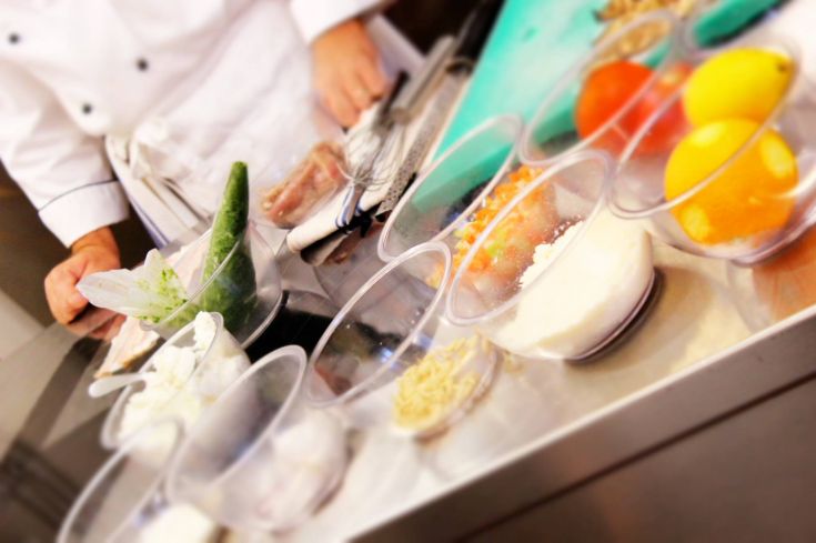 A cook organizes fresh ingredients on a countertop, surrounded by various foods in containers.