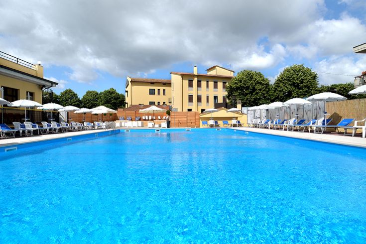 Una piscina di colore blu, circondata da lettini e ombrelloni, con un edificio che si trova sullo sfondo.