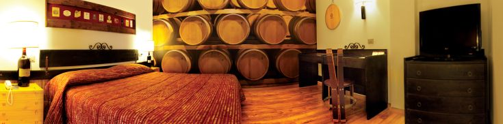 Hotel Giò Zimmer mit warmfarbigen Möbeln und einladend angeordneten Holzfässern.
