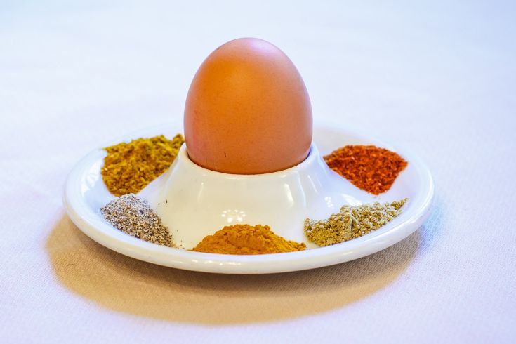 An egg placed on a small dish, surrounded by various brightly colored spices.