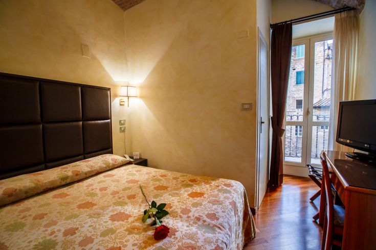 Simple room with a double bed and floral decorations, overlooking historic balconies.