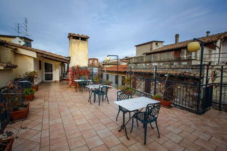 A hotel terrace furnished with small tables and plants, surrounded by historic buildings.