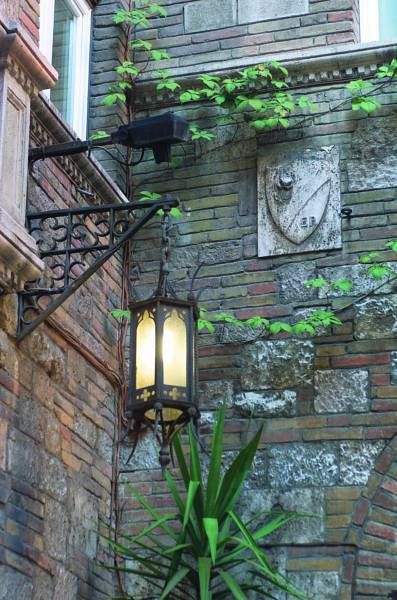 Lampione in ferro su un muro in mattoni, circondato da vegetazione verde.