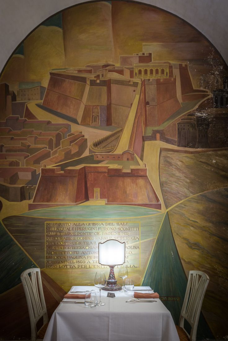 Interno di un ristorante con un muro in tufo decorato e un tavolo ben apparecchiato, ambiente silenzioso e gradevole.