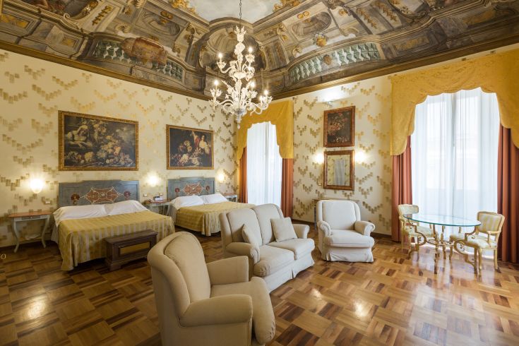 Stanza di un albergo storico con arredi classici e un lampadario che diffonde una luce calda.