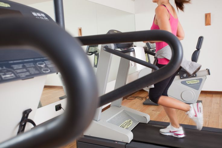 A woman runs on a treadmill in a well-equipped gym, focusing on exercise and wellness.