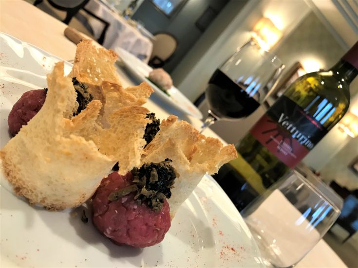 A gourmet dish with meat, served with crostini and red wine, in an elegant setting.