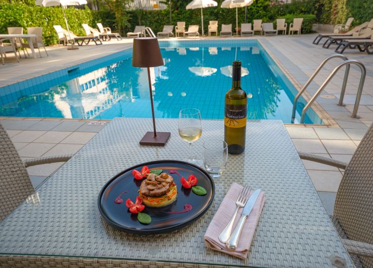 Casual lunch by the pool with simple dishes and wine, next to a blue water pool.