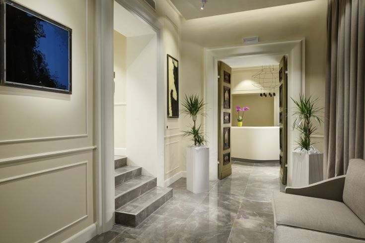 Hotel corridor with natural light, adorned with plants and simple details, leading to bright interior spaces.