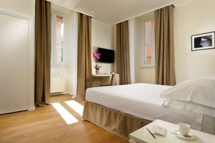 A bright and simple hotel room with wooden floors and large windows allowing natural light.