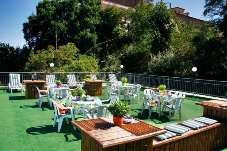 Außenbereich des Gebäudes mit Tischen und Liegen in einer grünen, entspannten Umgebung.