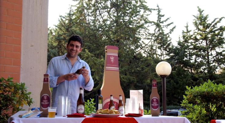 Ein lächelnder Mann serviert Bier und Snacks in einer grünen und entspannten Umgebung.