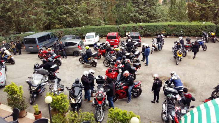 Ein Parkplatz für Motorräder und Autos, umgeben von Grünflächen, leicht überfüllt.