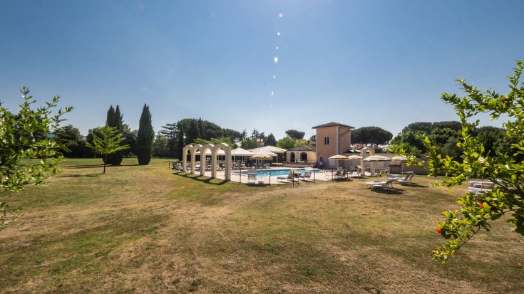A hotel surrounded by trees, featuring a pool and relaxation areas, located between two Umbrian cities.