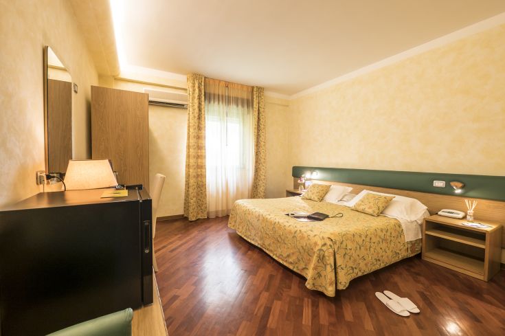 Simple and functional hotel room with light-colored furniture and modern comforts; a peaceful environment in the Umbria region.