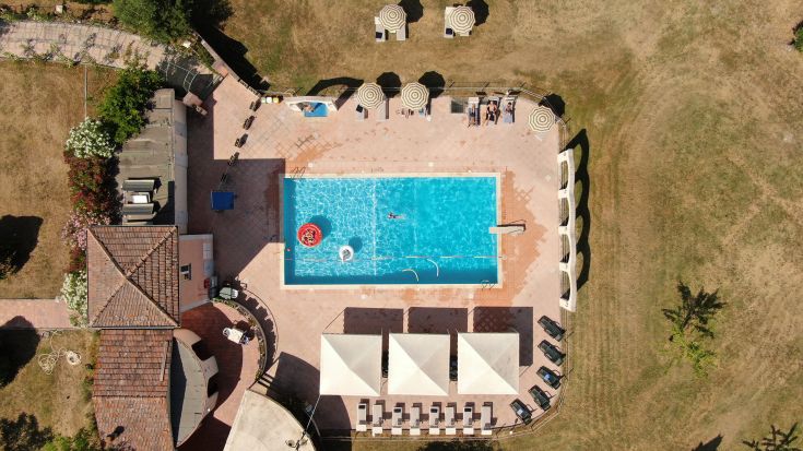 A view of a swimming pool surrounded by sunbeds and umbrellas, nestled in the surrounding greenery.