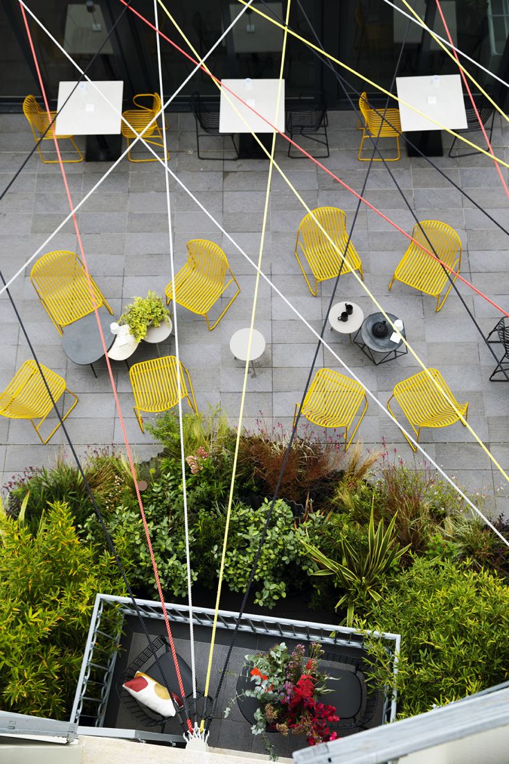 Spazio esterno con sedie gialle e tavoli, decorato con piante e fili colorati.